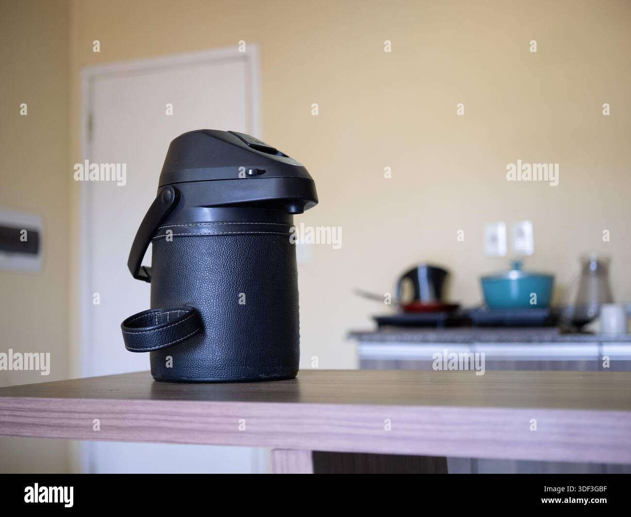 Fiasca termica nera su un tavolo con sfondo sfocato in cucina, che rappresenta bevande calde e routine domestica. Foto Stock