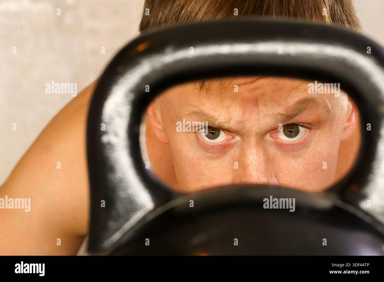 Uomo con occhi determinati attraverso il kettlebell. Primo piano di un atletico con uno sguardo intenso visibile attraverso il manico kettlebell Foto Stock