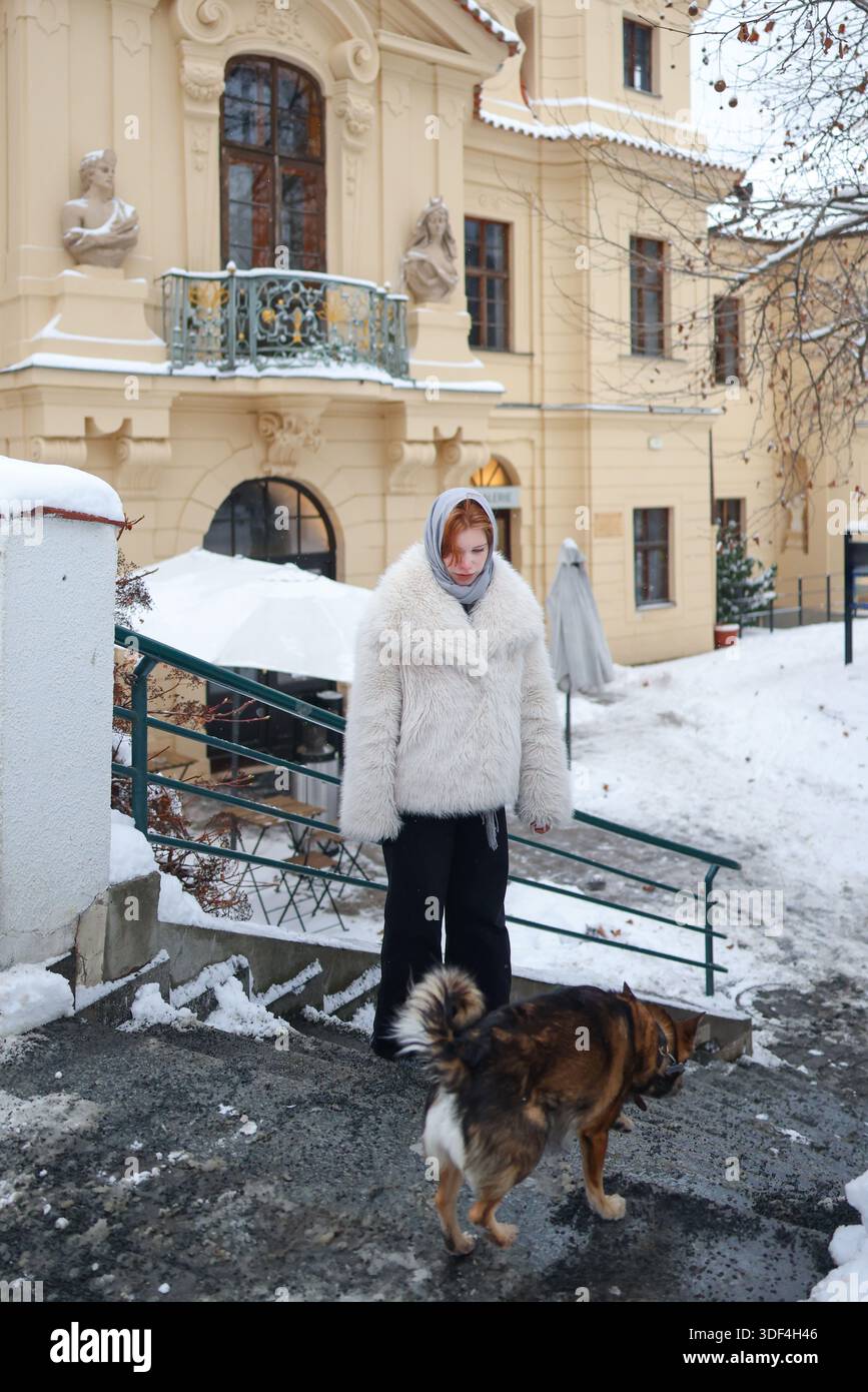Donna che cammina in una strada innevata vicino a un edificio storico, stile di vita invernale e routine quotidiana Foto Stock