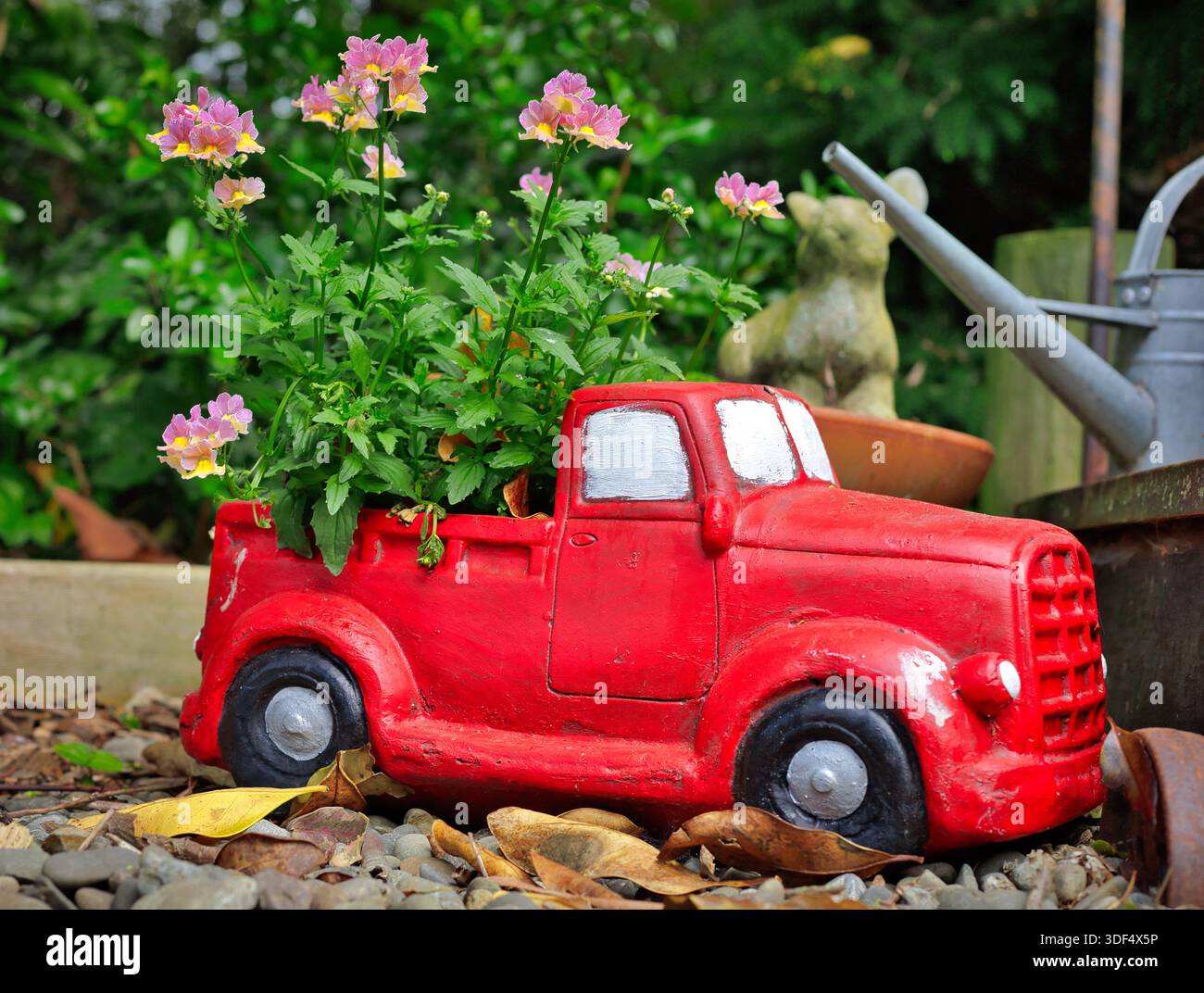 Meraviglioso modello di veicolo da giardino rosso brillante con un impianto di fioritura. Foto Stock