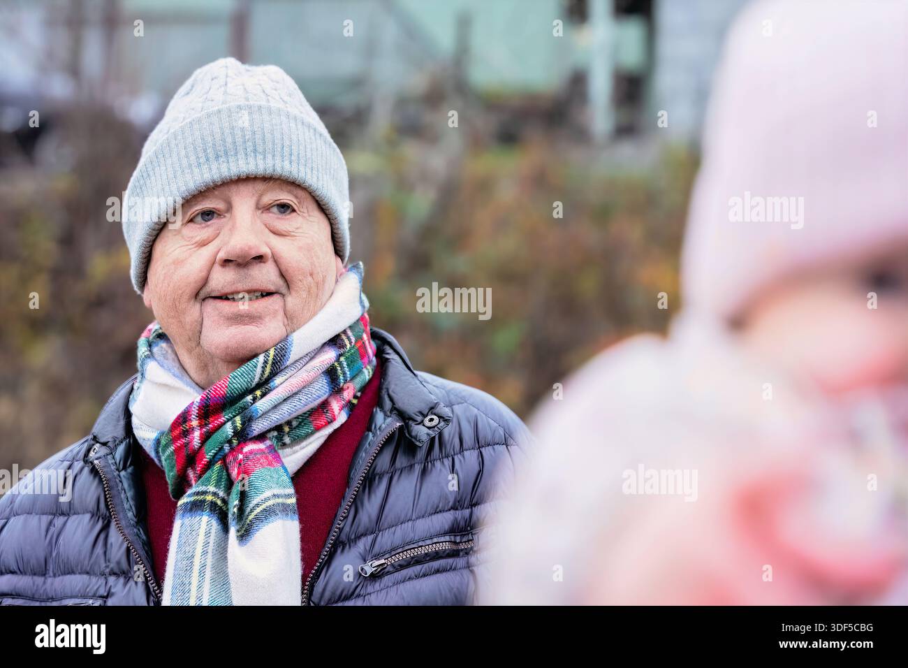 Uomo anziano vestito con abiti caldi, sorridente in un ambiente all'aperto, circondato dalla natura, catturando un'atmosfera allegra durante il freddo Foto Stock