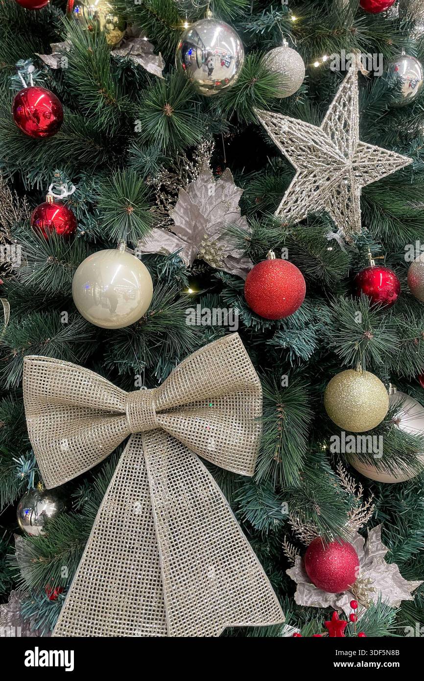 Decorazioni scintillanti per il nuovo anno appese sull'albero di Natale verde, palle e archi argentati e rossi Foto Stock