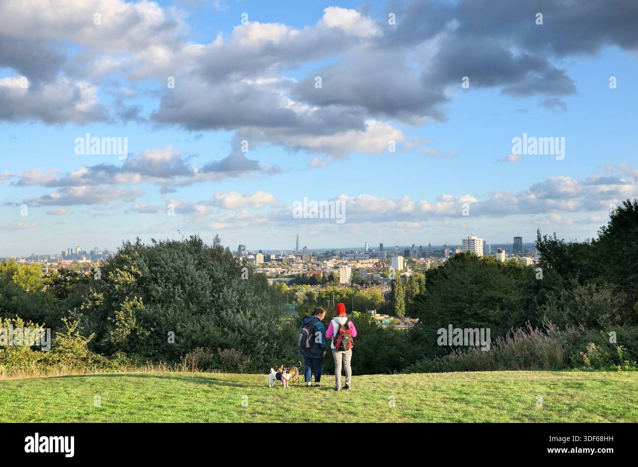 Due donne con cani si fermano per un momento per ammirare la vista su Parliament Hill che si affaccia sullo skyline di Londra, Hampstead Heath, Londra, Inghilterra, Regno Unito. Foto Stock