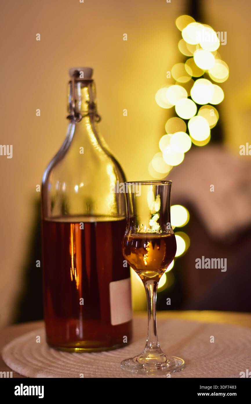 Bottiglia e bicchiere di brandy davanti a sfocate luci natalizie Foto Stock