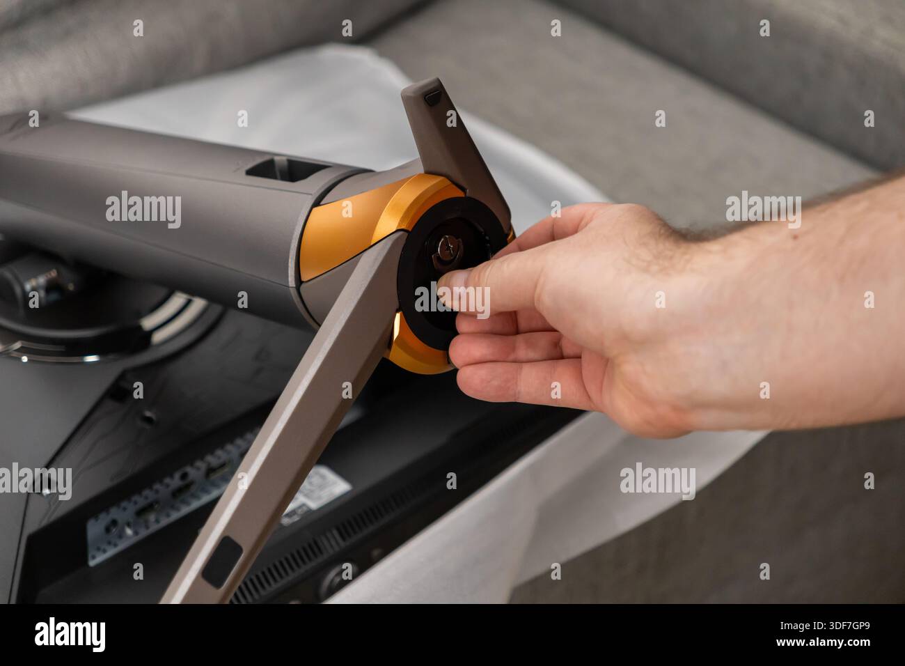 Primo piano di una mano serrando con cura una vite sulla base di un supporto per monitor da gioco high-tech, garantendo un assemblaggio stabile e la disponibilità per una pe ottimale Foto Stock