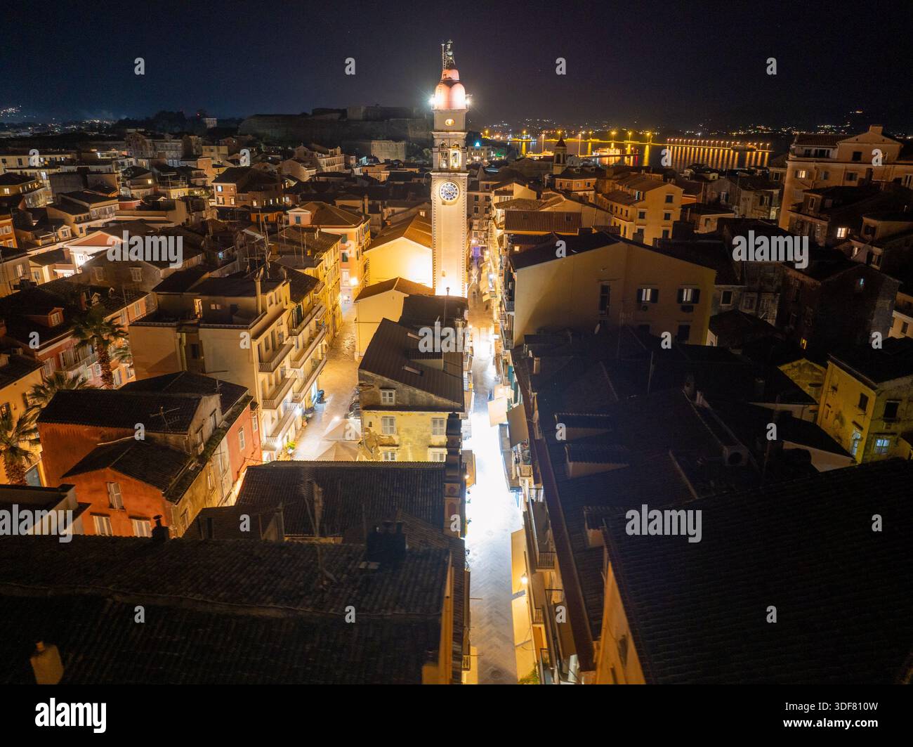 Vista verticale aerea del campanile illuminato della chiesa di San Spyridon che si innalza sopra i tetti scuri della città vecchia di Corfù durante la notte di Pasqua Foto Stock