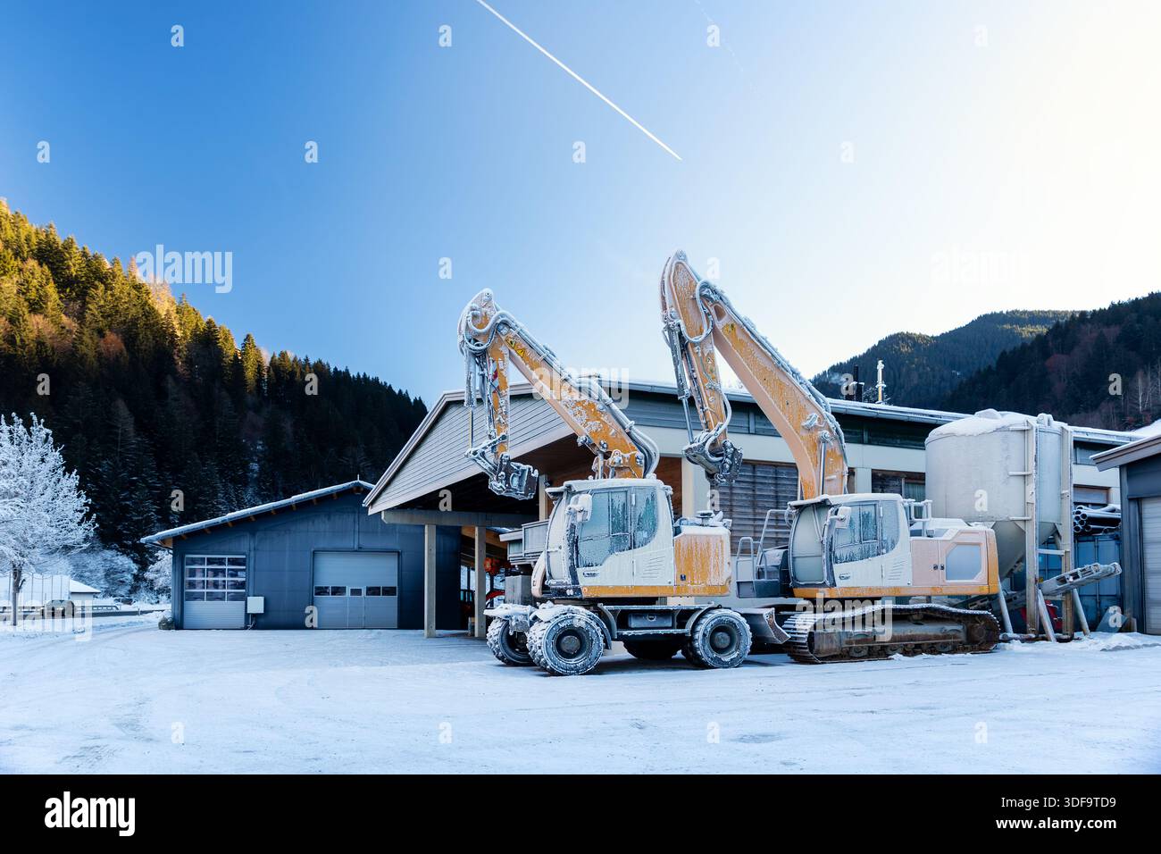 Vista panoramica escavatori idraulici congelati all'aperto condizioni invernali neve coperta ghiaccio industriale edificio alpino. Impatti a basse temperature Foto Stock