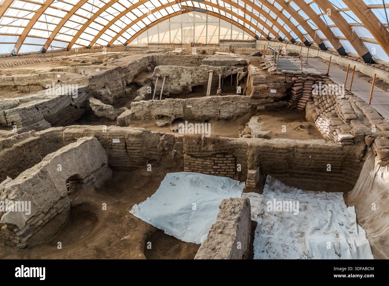 I muri a strati di case in mattoni di fango di Çatalhöyük, una delle più famose colonie neolitiche del mondo, sono esposti sotto un riparo con struttura in legno vicino al villaggio di Küçükköy, in Turchia. Sacchi di sabbia e fogli di plastica proteggono i fragili resti, vecchi di circa 9.000 anni, formatisi nel corso di più di mille anni di ricostruzione continua sullo stesso sito. Foto Stock