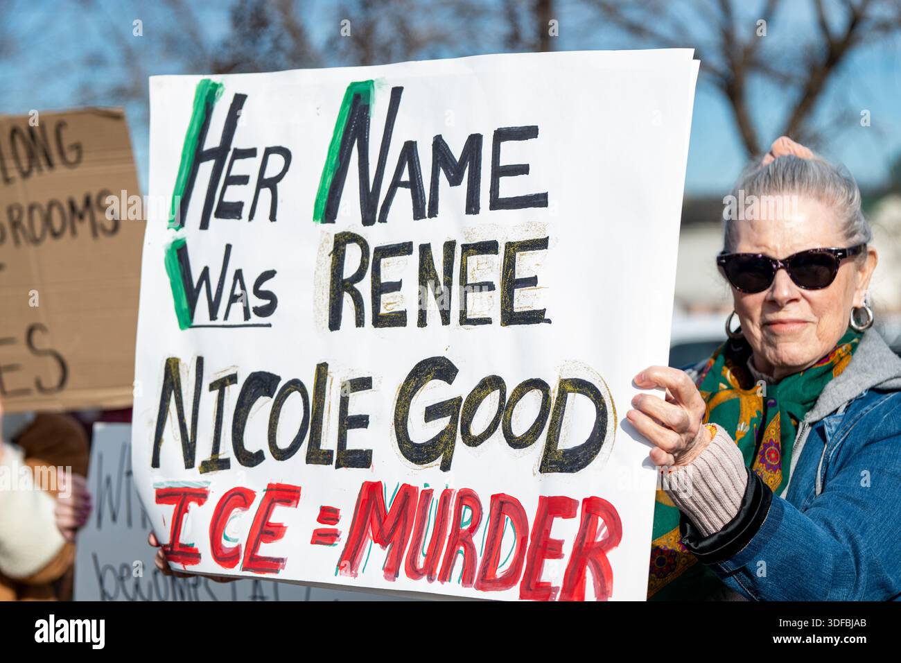 Una donna guarda la telecamera mentre tiene in mano un cartello di protesta fatto a mano che recita "il suo nome era Renee Nicole buono" e "ICE = omicidio" in lettere rosse. Foto Stock