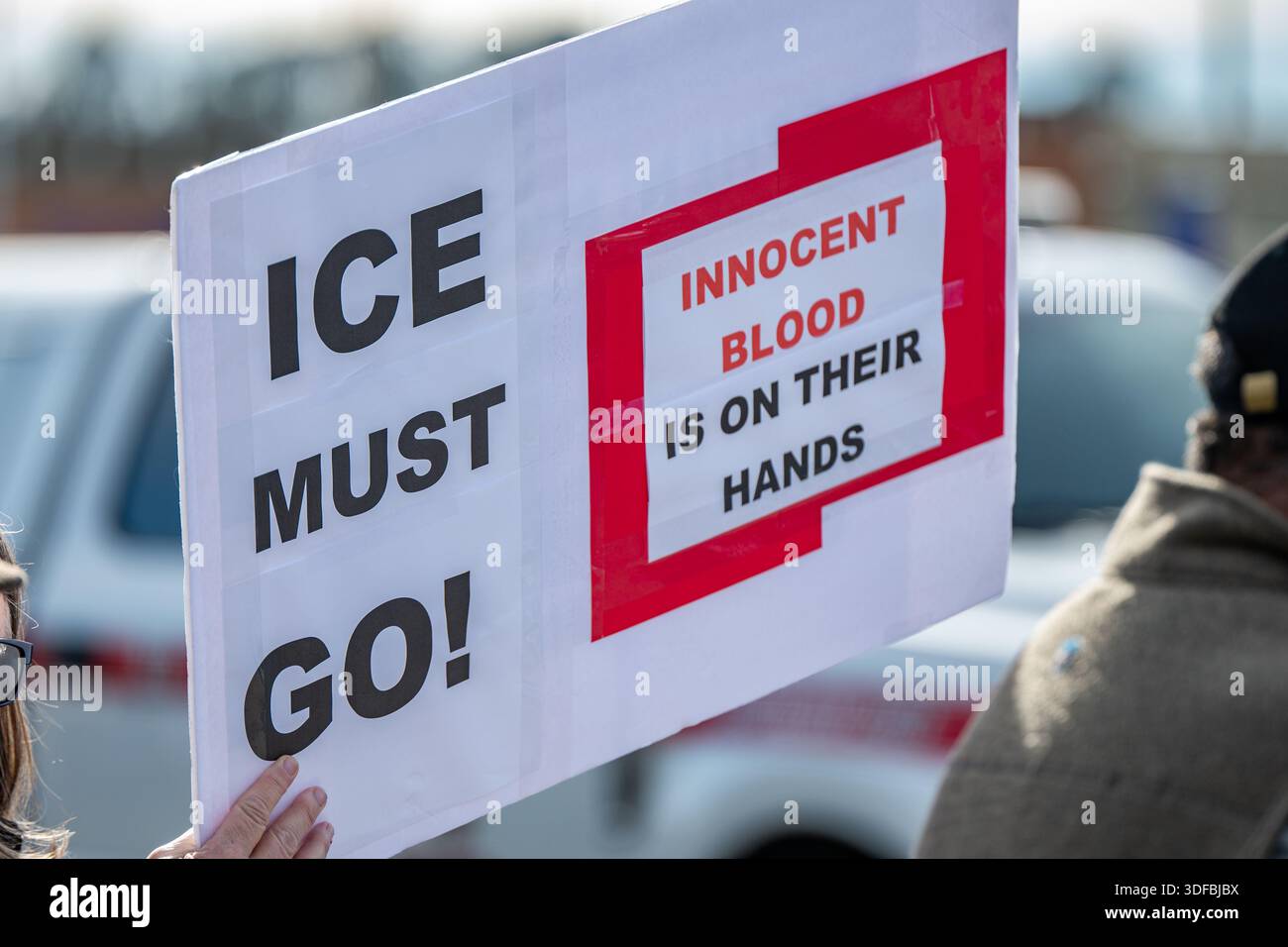 Un cartello di protesta fatto a mano con la scritta "ICE must go". Sangue innocente sulle loro mani è trattenuto da un dimostrante mentre un'auto passa in un rally stradale. Foto Stock