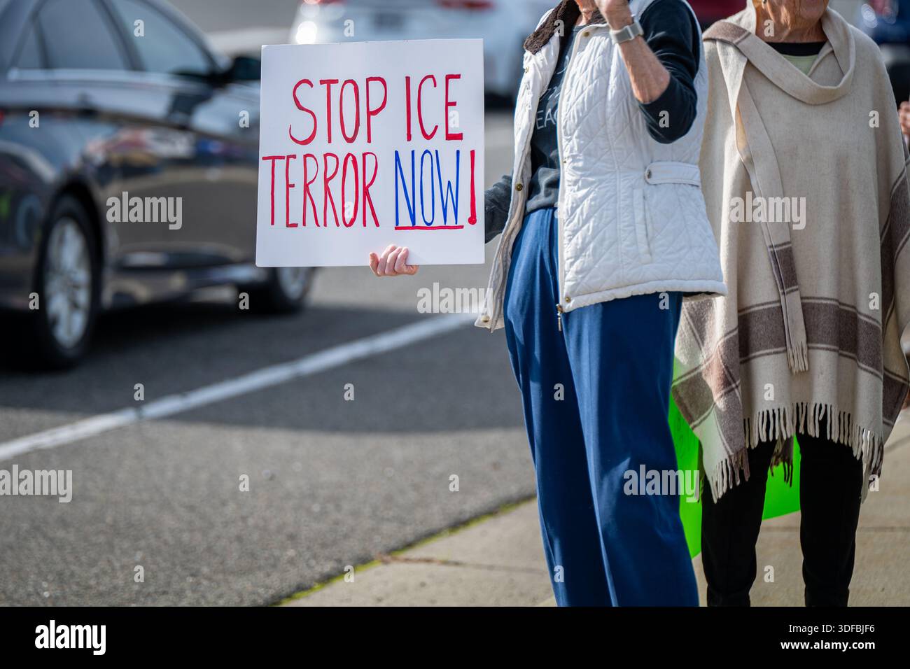 Una donna si trova lungo il lato di Bell Road con un cartello "Stop ICE Terror Now" mentre un veicolo passa davanti durante una dimostrazione locale Foto Stock