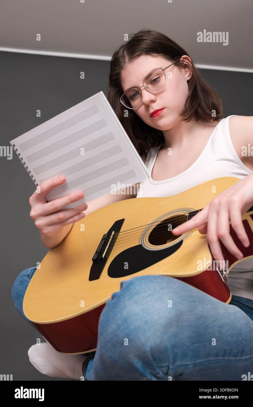 La musicista donna tiene spartiti davanti a lei, decifrando e analizzando la nuova creazione musicale nel processo creativo durante le prove. Giovane chitarrista Foto Stock