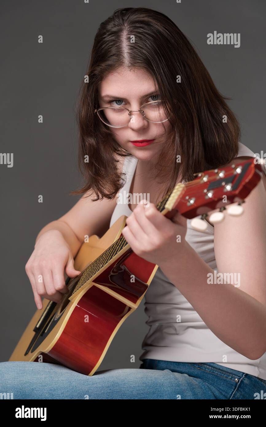 La musicista rock suona la classica chitarra acustica a sei corde, eseguendo un brano musicale tecnicamente impegnativo. Giovane donna adulta chitarrista noi Foto Stock