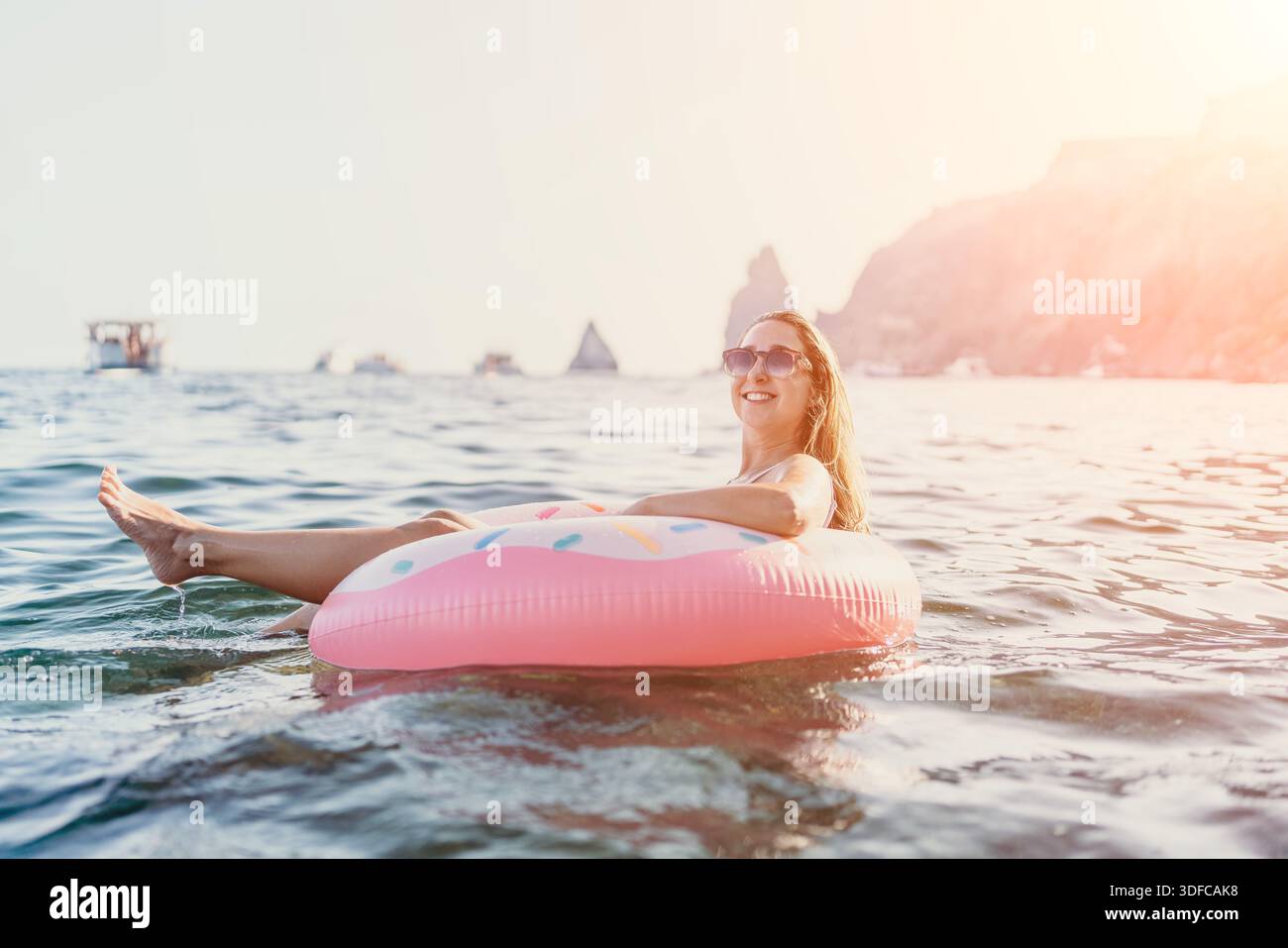 Donna, galleggiante, mare. Donna felice che si gode le vacanze estive su un anello di ciambelle gonfiabile in un mare calmo con scogliere, spazio copia. Foto Stock