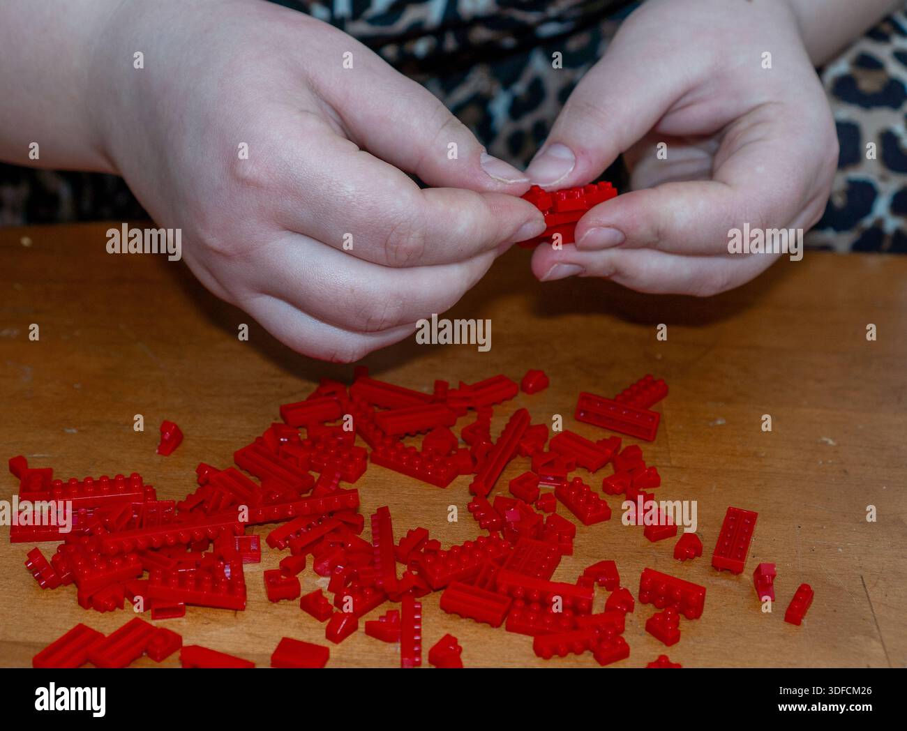 Primo piano delle mani assemblaggio di pezzi di bloccaggio in plastica rossa Foto Stock