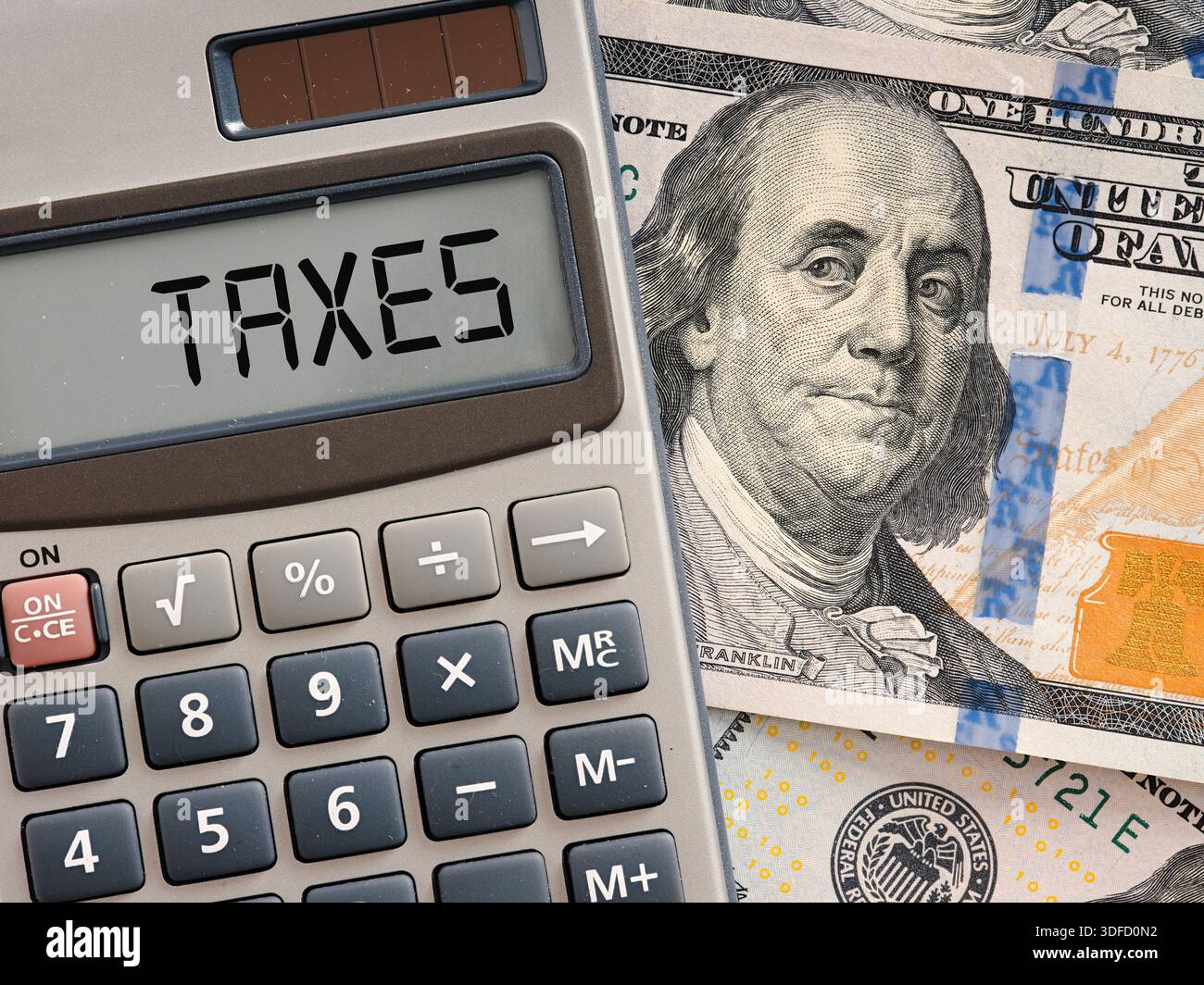 Calcolatrice che mostra la parola tasse sul suo schermo che si trova sopra le banconote americane da cento dollari. Concetto fiscale e fiscale. Foto Stock