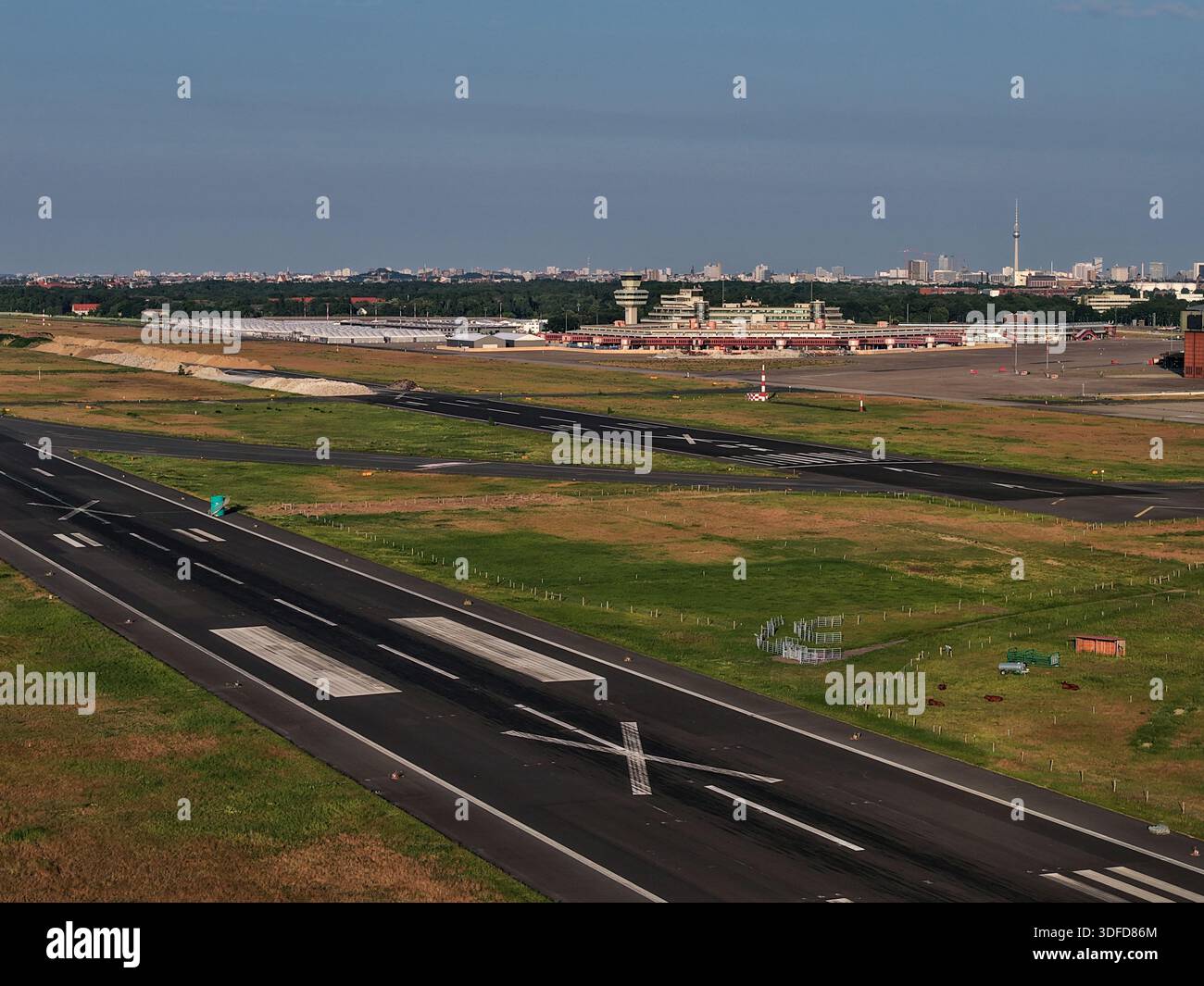 La vista aerea della pista si estende verso la torre di controllo di Berlino, Berlino, Germania, segnata da linee bianche e dure contro l'asfalto scuro. Foto Stock
