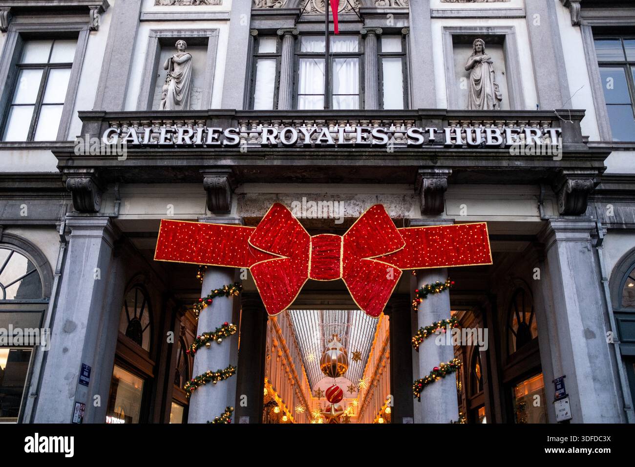 Vista frontale dell'ingresso alle Galeries Royales Saint Hubert, decorato con un gigantesco arco di Natale rosso e luci a Bruxelles capitale a Belg Foto Stock