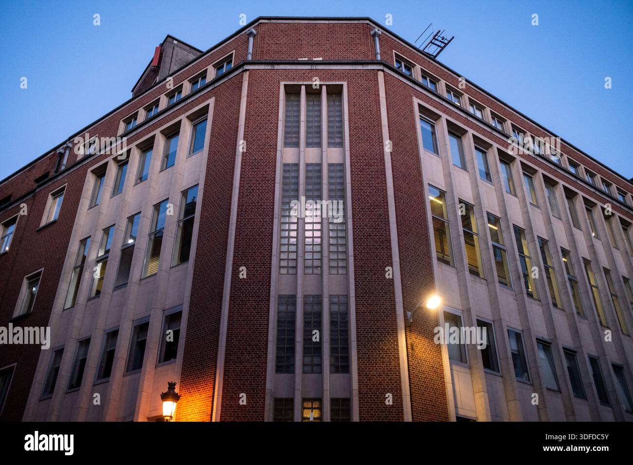 Vista architettonica dell'edificio della scuola di comunicazione IHECS illuminato al crepuscolo con lampioni e finestre che si illuminano a Bruxelles capitale in B. Foto Stock