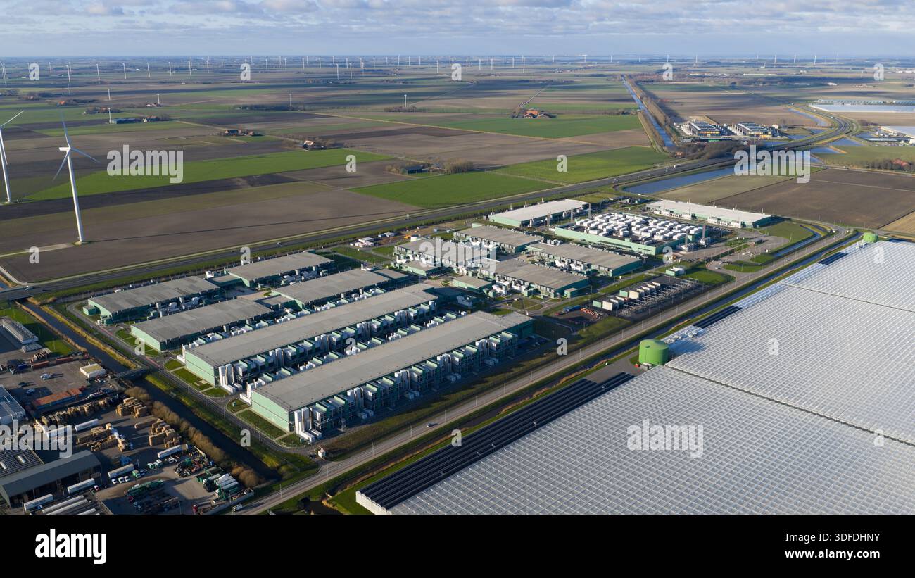 Vista aerea di file di edifici industriali in contrasto con i campi aperti punteggiati di turbine eoliche, Agriport, Middenmeer, Paesi Bassi. Foto Stock