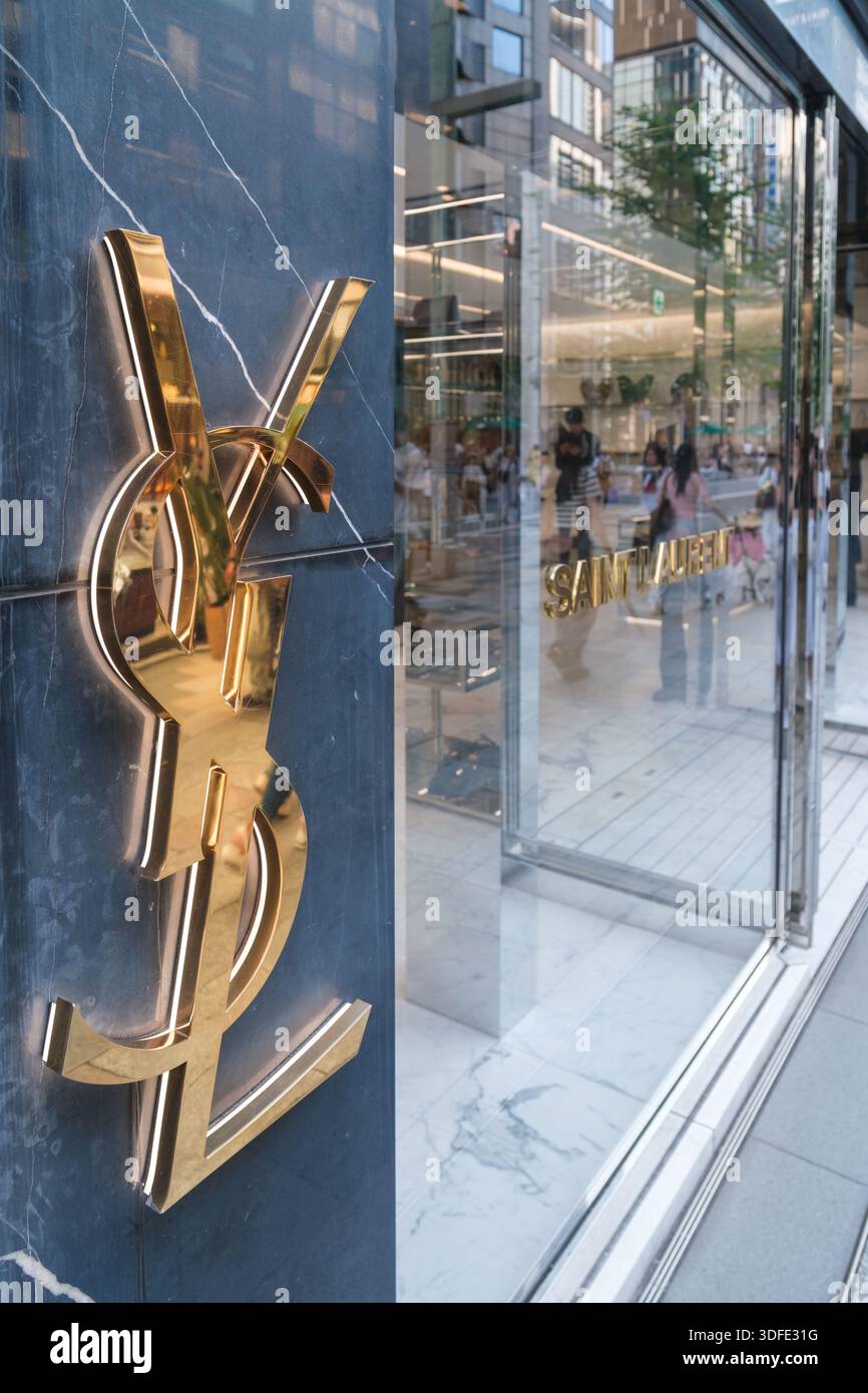 Tokyo, Giappone - 09 agosto 2025: Logo YSL dorato in evidenza sull'esterno del negozio di lusso, che cattura i riflessi stradali in un vivace quartiere di Ginza Foto Stock