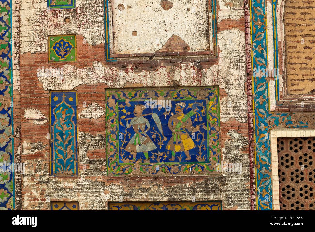 Vista di intricate piastrelle raffiguranti figure adornano una parete di mattoni intemprati, che mostra una miscela di colori e texture sbiaditi, Lahore, Punjab, Pakistan. Foto Stock