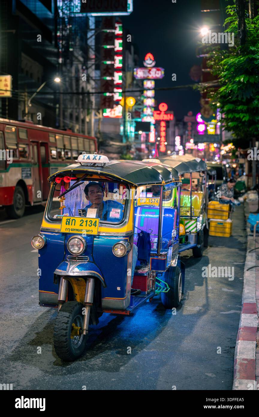 Bangkok, Tailandia - 11.11.2025: Tuk tuk in attesa su Yaowarat Road nella Chinatown di Bangkok di notte, con insegne al neon lucenti alle spalle e turisti che camminano al mattino Foto Stock