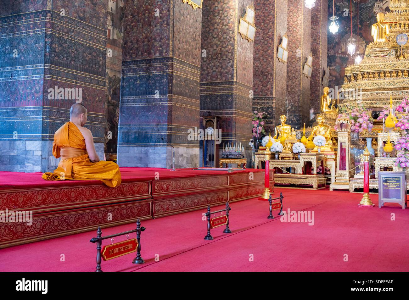 Bangkok, Tailandia - 11.11.2025: Monaco buddista in abiti tradizionali arancioni seduto all'interno di un tempio e pregando in silenzio, creando una calma spirituale sc Foto Stock