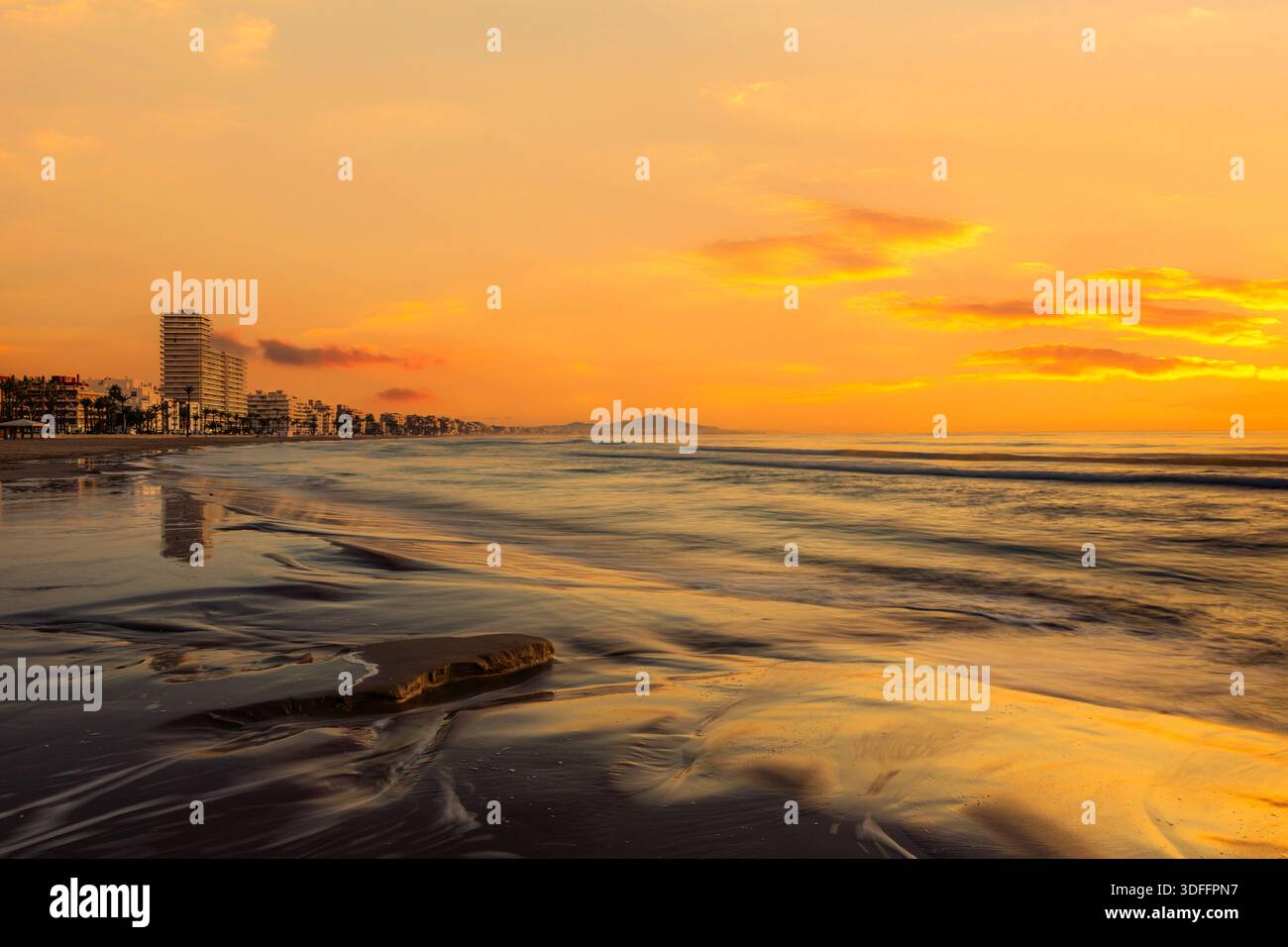 L'alba dipinge il cielo mentre il mare calmo e la sabbia bagnata riflettono colori caldi, Peniscola, Spagna Foto Stock