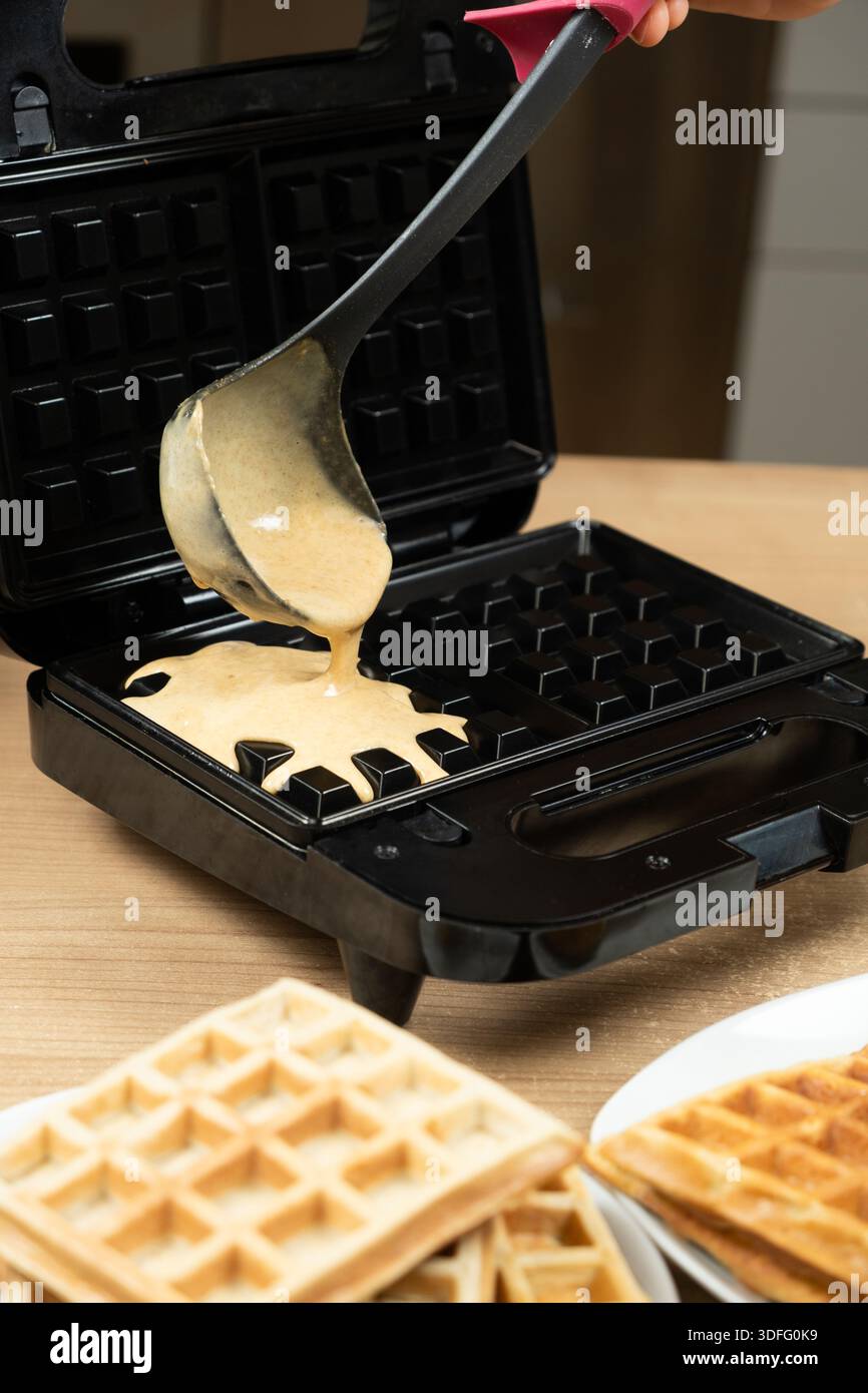Versare la pastella di waffle freschi con una malilla in una macchina per waffle elettrica nera Foto Stock