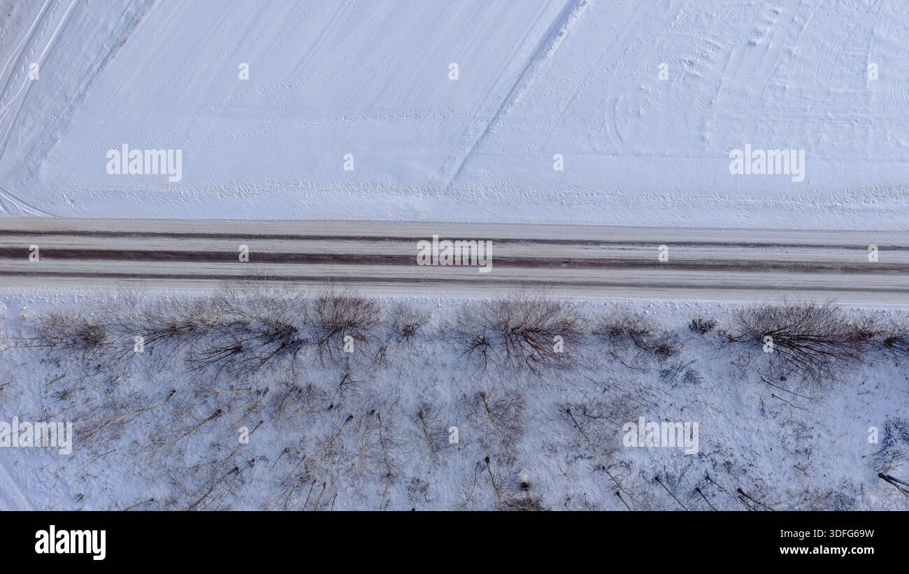 Vista dall'alto dall'alto di una strada rettilinea a due corsie a Nowy Lubiel, Polonia, che taglia la neve, con campi arati sopra e arbusti sparti senza foglie e. Foto Stock