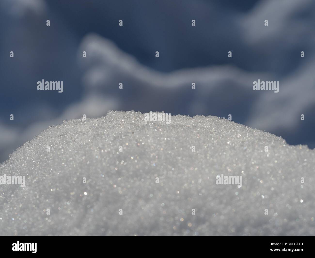 Un primo piano di un tumulo di neve scintillante contro un cielo azzurro, catturando la micro texture dei cristalli di ghiaccio e l'atmosfera fresca e tranquilla dell'inverno all'aperto Foto Stock