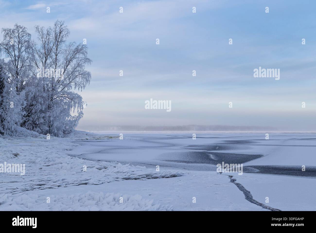 Alberi innevati e cumuli di ghiaccio e forme astratte su un lago ghiacciato e innevato in Finlandia in inverno di giorno. Splendido paesaggio naturale e tranquillo d'inverno Foto Stock