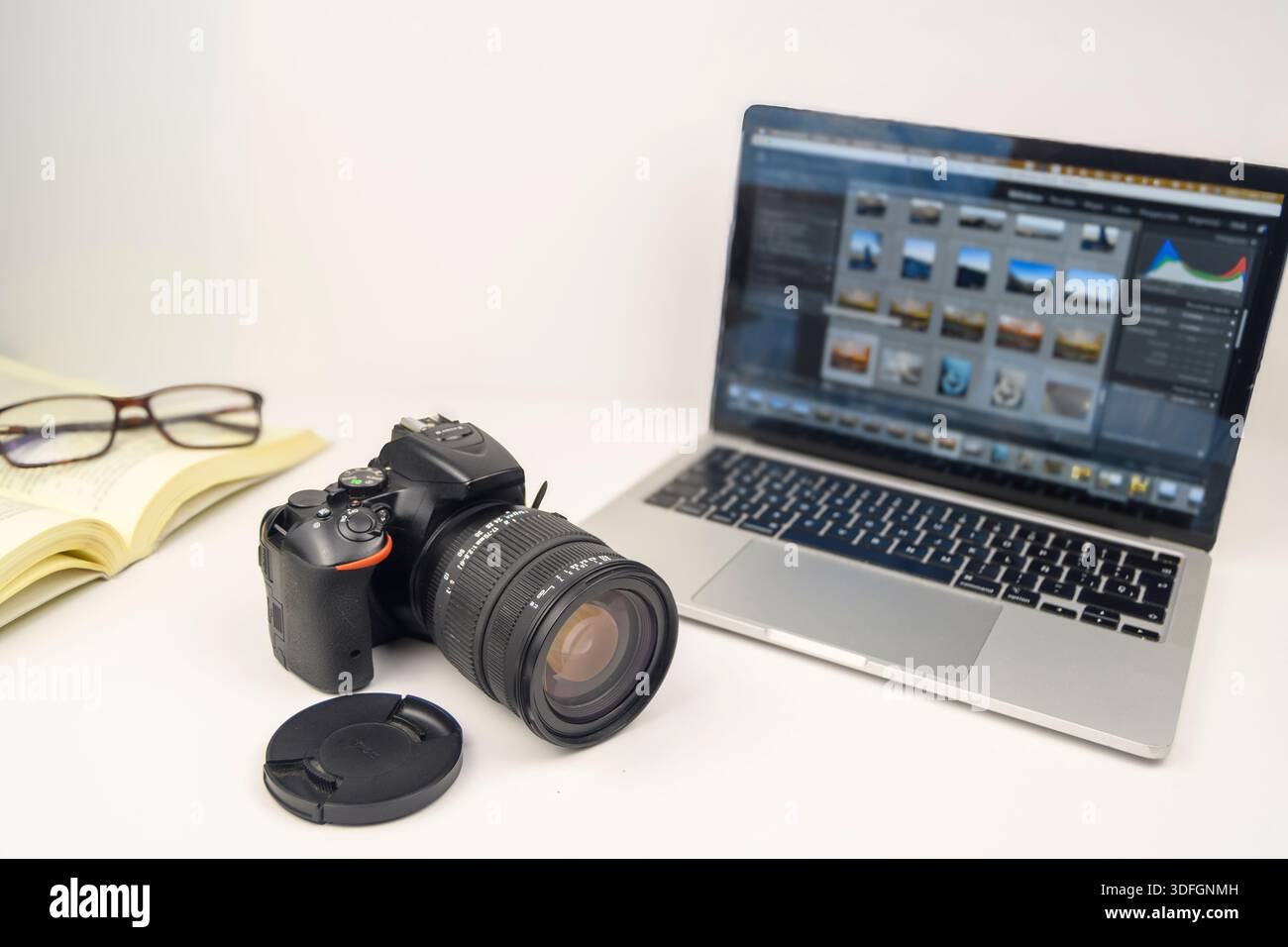 Area di lavoro per l'editing di foto con fotocamera DSLR, laptop che mostra la galleria di immagini, notebook e occhiali aperti, apprendimento creativo e concetto di post-produzione. Foto Stock