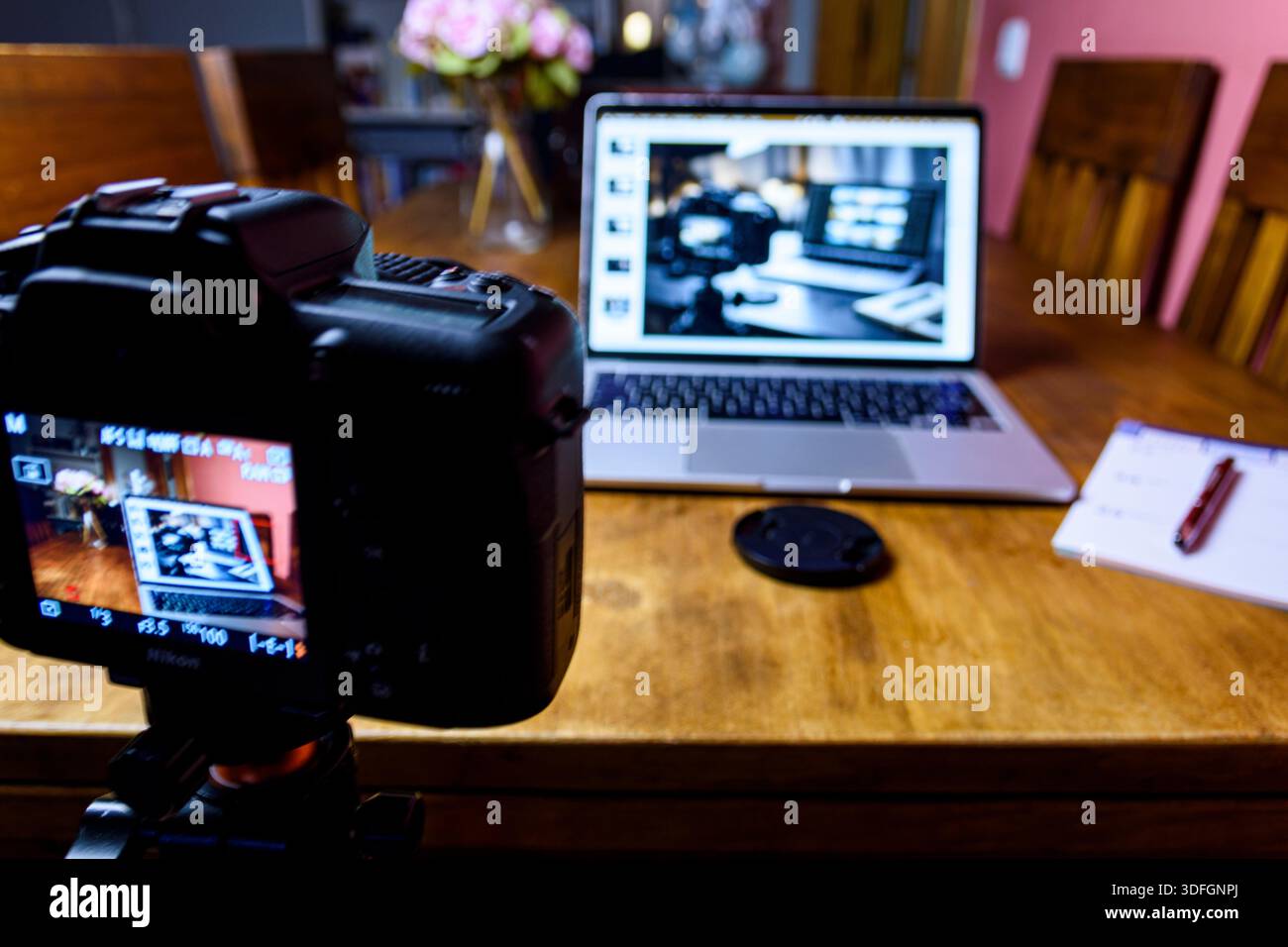 Studio domestico dietro le quinte: Fotocamera su treppiede che filma un computer portatile con editing di foto su un tavolo di legno. Spazio di lavoro ideale per i creatori con notebook. Foto Stock