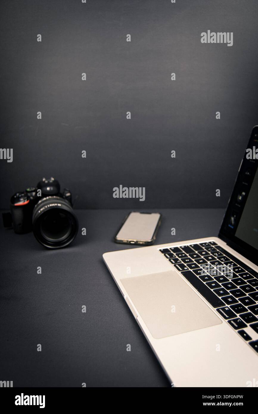 Scrivania minimalista scura con fotocamera, bordo del computer portatile e schermo vuoto per smartphone, ampio spazio negativo per testo e layout di design. Foto Stock