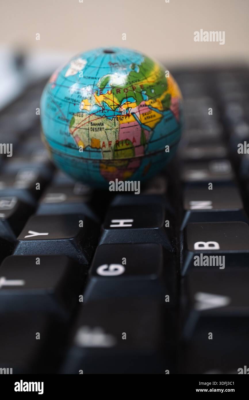 Un piccolo globo posizionato su una tastiera per computer, che mette in evidenza Africa ed Europa, simboleggiando la connettività e la tecnologia globali Foto Stock