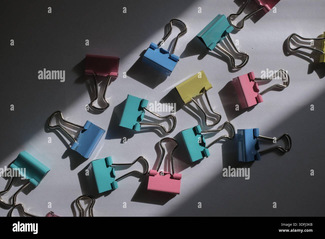Una raccolta di clip colorate sparse su una superficie, con ombre che proiettano la luce del sole Foto Stock