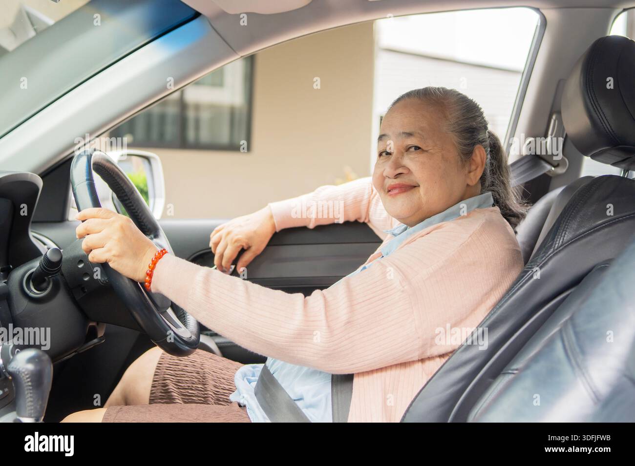 Donna asiatica sorridente alla guida di un'auto che guarda alla fotocamera mentre si gode la libertà e il viaggio, mani sul volante. Foto Stock