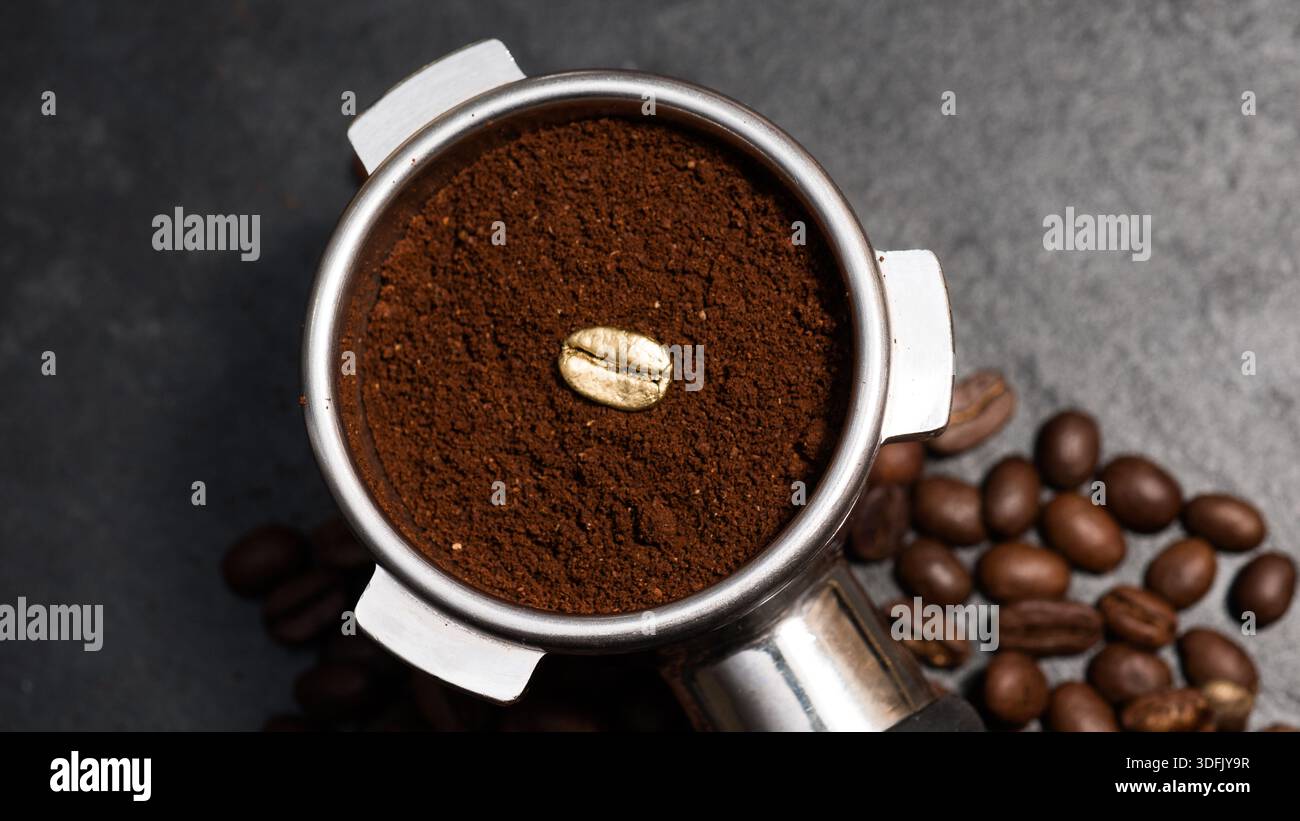 Portafiltro espresso riempito con caffè macinato con un unico chicco di caffè dorato, circondato da chicchi tostati e dorati su un bac di pietra scura Foto Stock