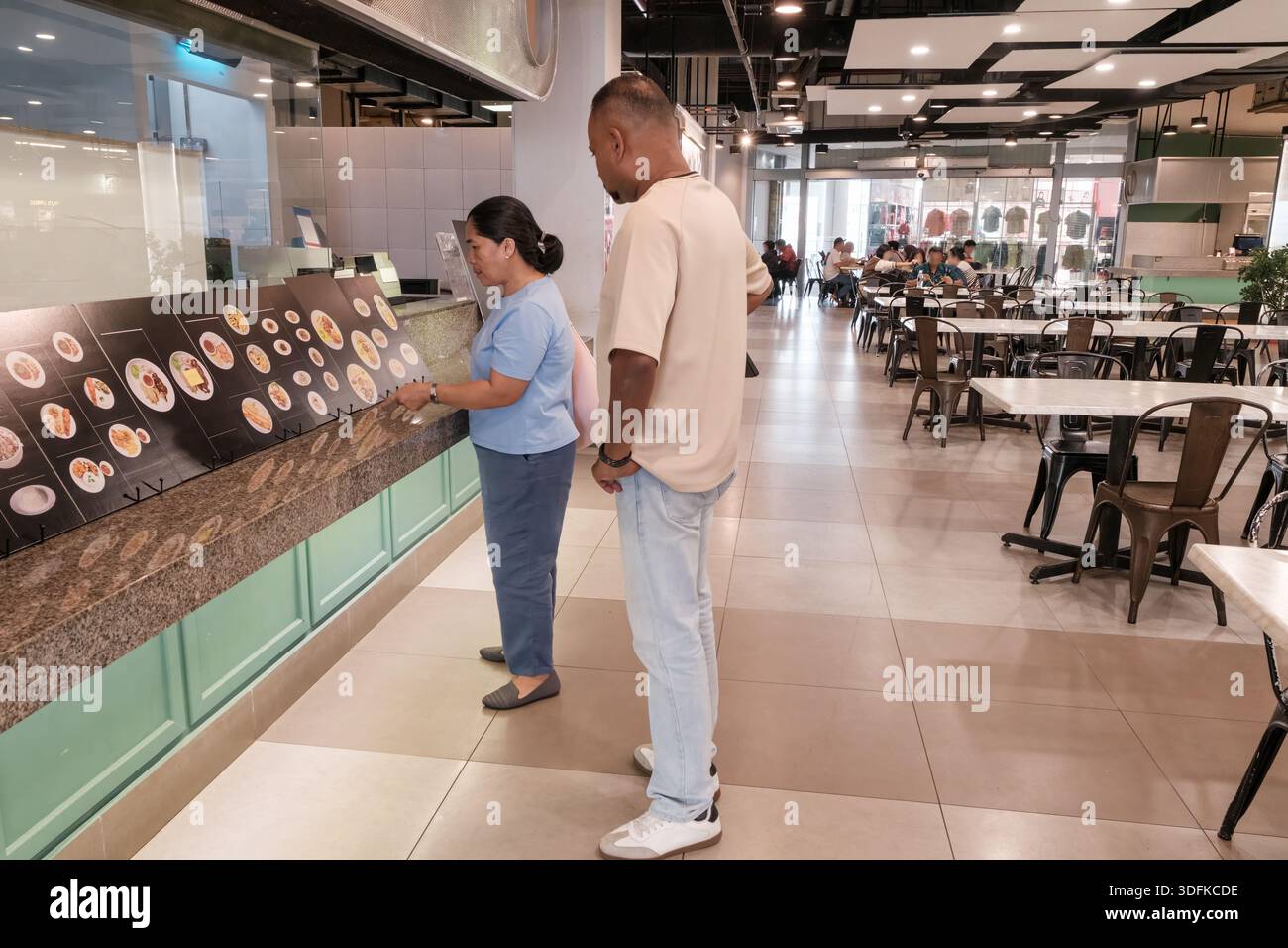 Un uomo e una donna stanno insieme, guardando un menu' in un ristorante. Le persone sono sedute ai tavoli sullo sfondo. E' ora di pranzo in un negozio Foto Stock