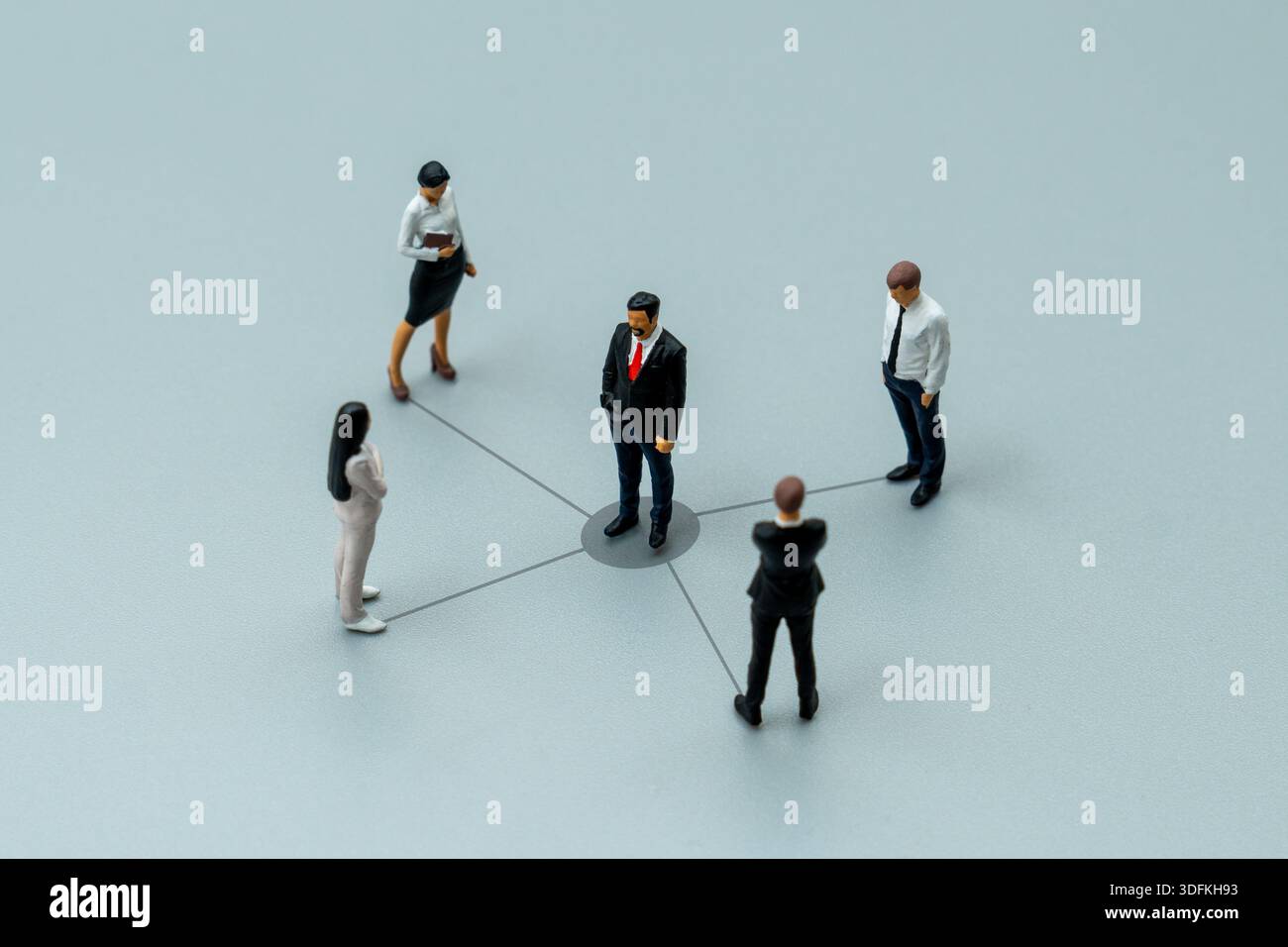 Persone in miniatura collegate da linee a un leader centrale. La delega dei compiti, la ripartizione delle responsabilità. Foto Stock