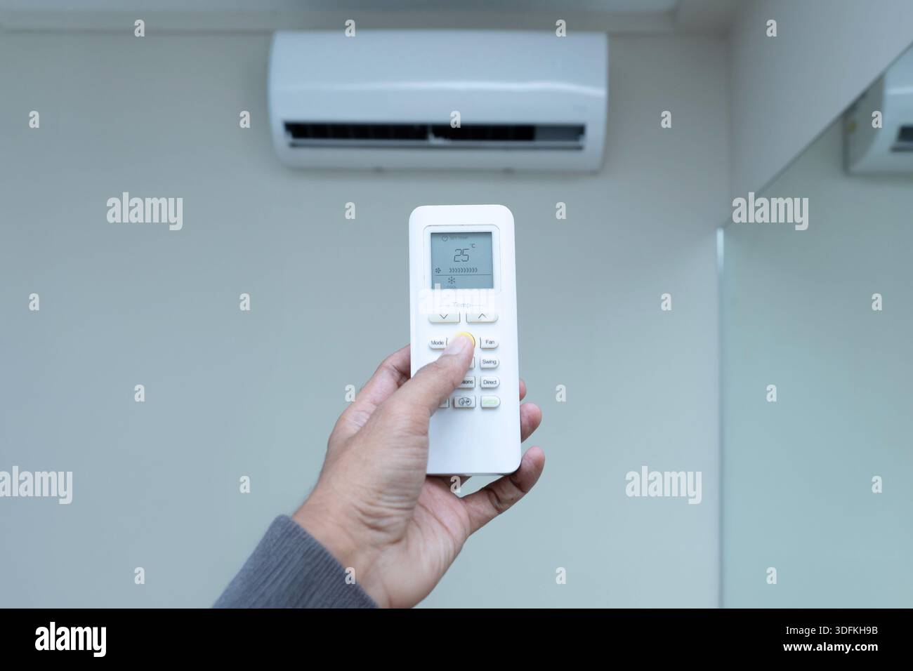 Una mano regge il telecomando del climatizzatore, impostando la temperatura a 25 °C per un livello di efficienza energetica. Climatizzatore, comfort domestico ed energia Foto Stock