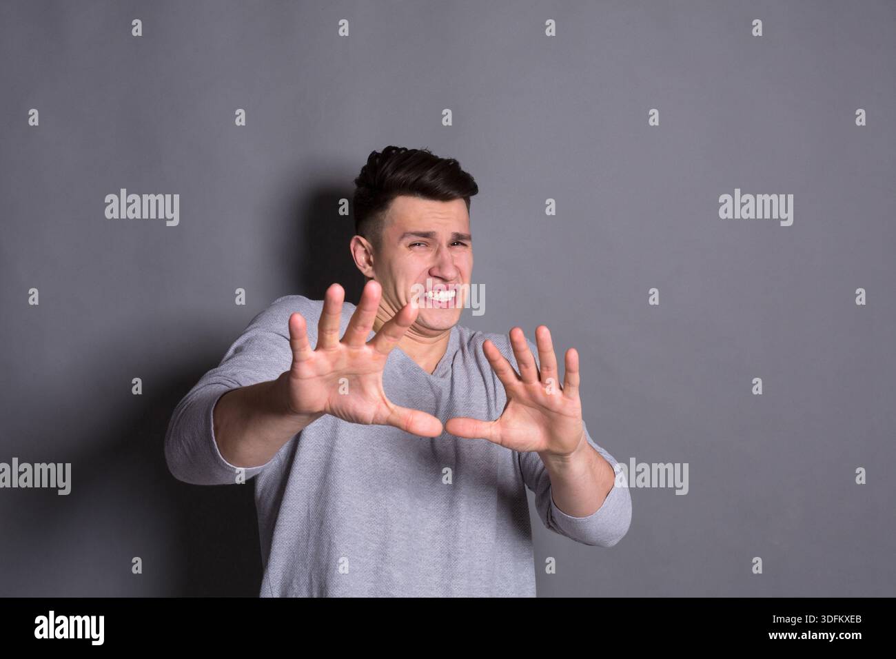 Uomo che esprime disagio mentre gesti con le mani su sfondo grigio Foto Stock