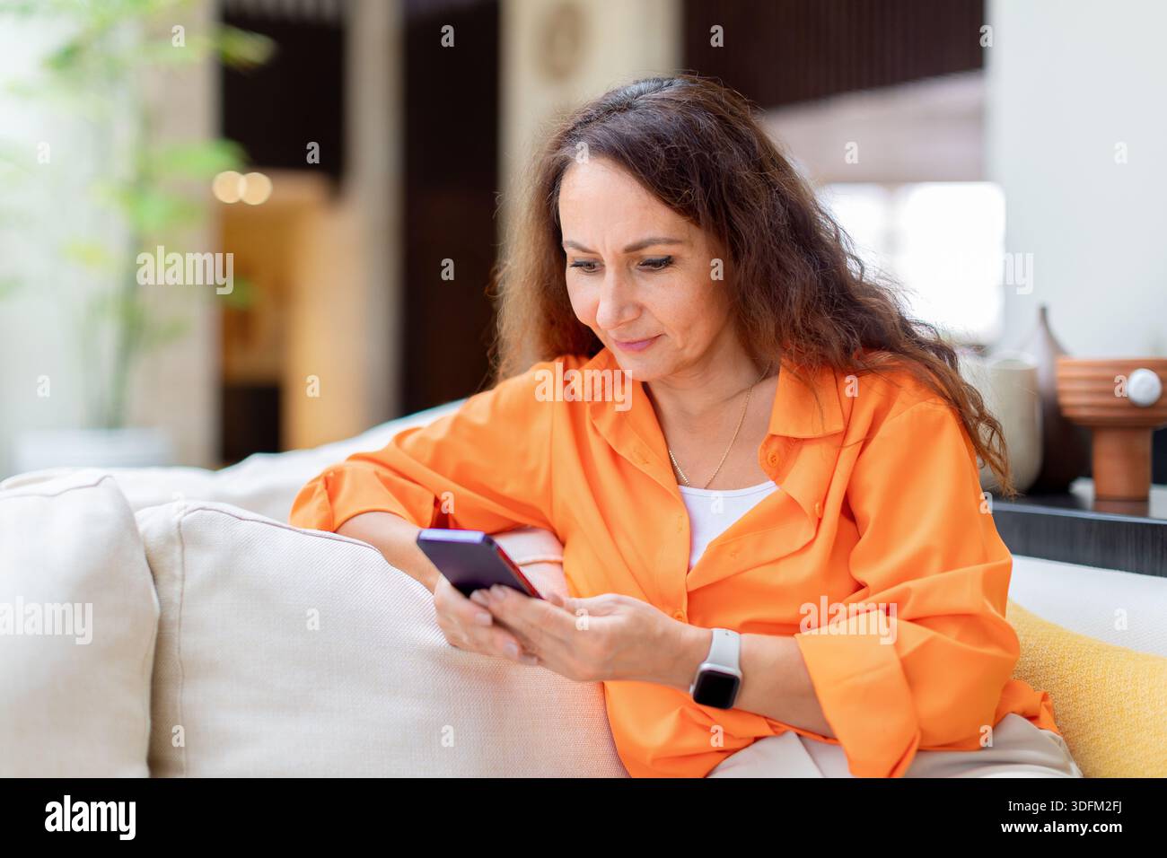 Donna caucasica premurosa che controlla i messaggi sullo smartphone mentre siede nella lounge dell'hotel Foto Stock