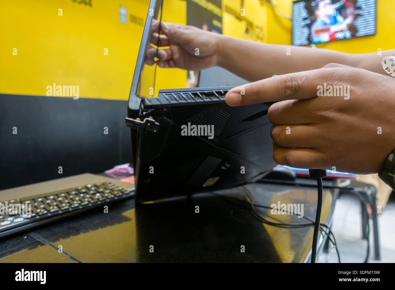 Un computer portatile MSI da gioco è tenuto da una persona che indica una sezione rotta vicino allo scarico della ventola posteriore, in un'officina di riparazione di computer. Cebu, Filippine Foto Stock