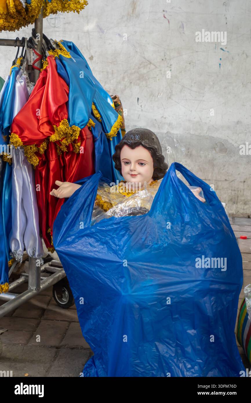 Statua del bambino Gesù, Santo Nino vestito con vesti colorati in sacchetto di plastica blu per il trasporto al negozio locale di Cebu, Filippine Foto Stock