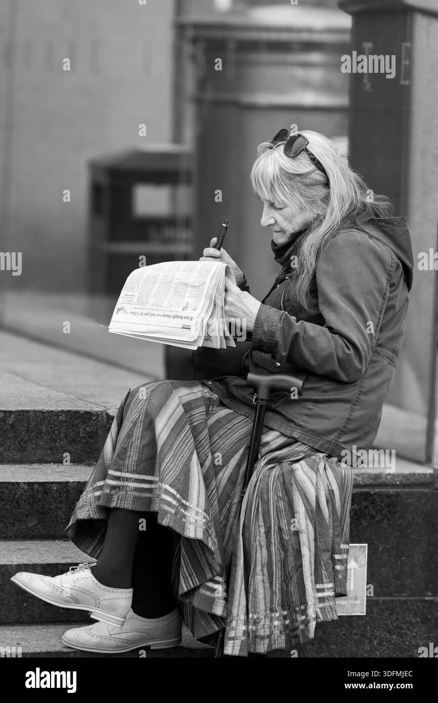 Donna premurosa che legge un giornale sui gradini urbani all'aperto, Leeds, West Yorkshire, Regno Unito. Foto Stock