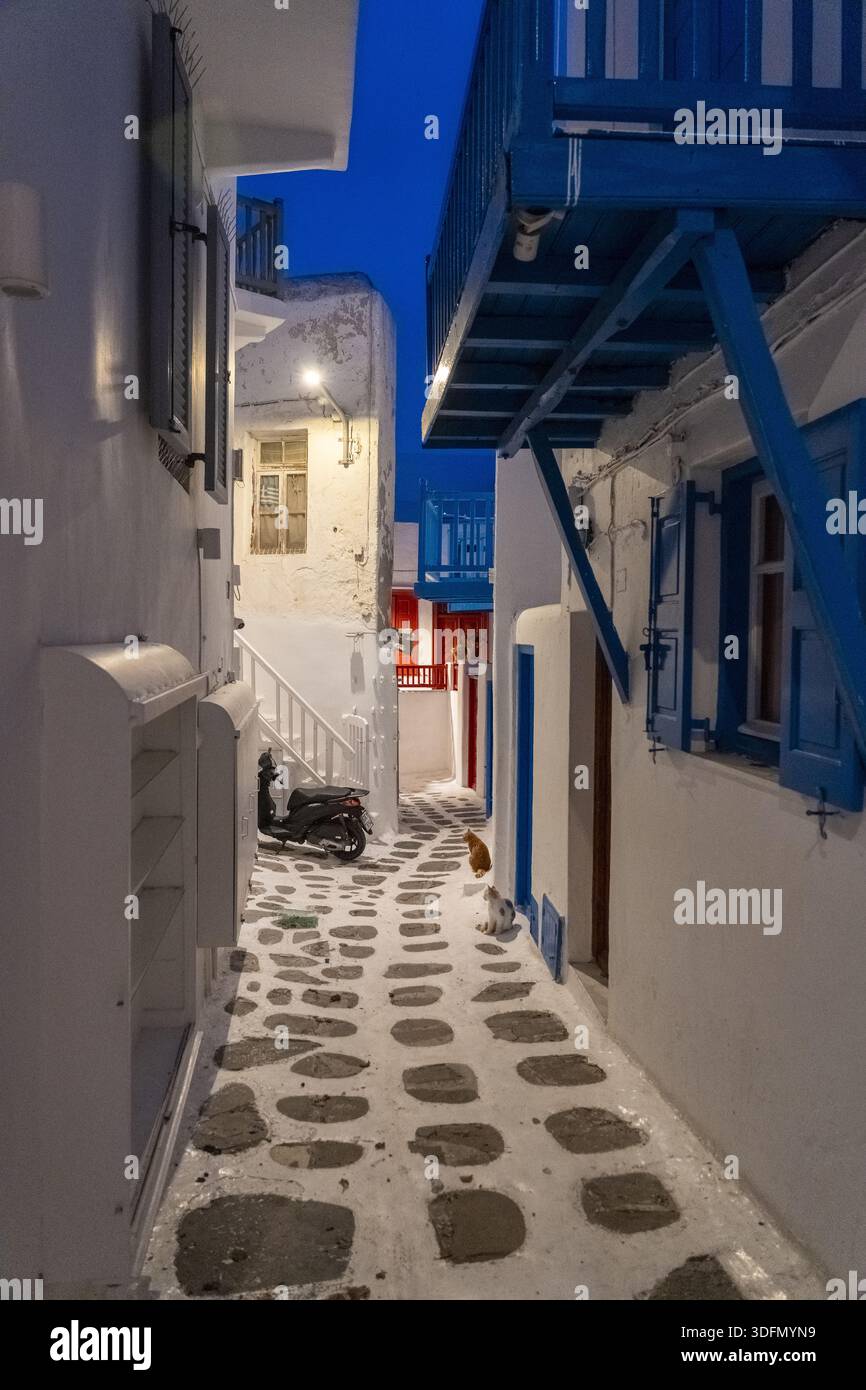Vista di una pittoresca e stretta strada lastricata di pietre bianche, fiancheggiata da edifici imbiancati con accenti blu vibranti sotto il cielo blu profondo, Mykonos, Foto Stock
