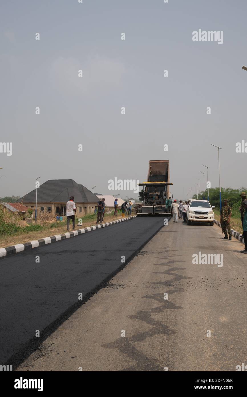 Lavoratori della costruzione di strade che posano asfalto fresco su una strada suburbana durante il progetto di sviluppo delle infrastrutture. Foto Stock